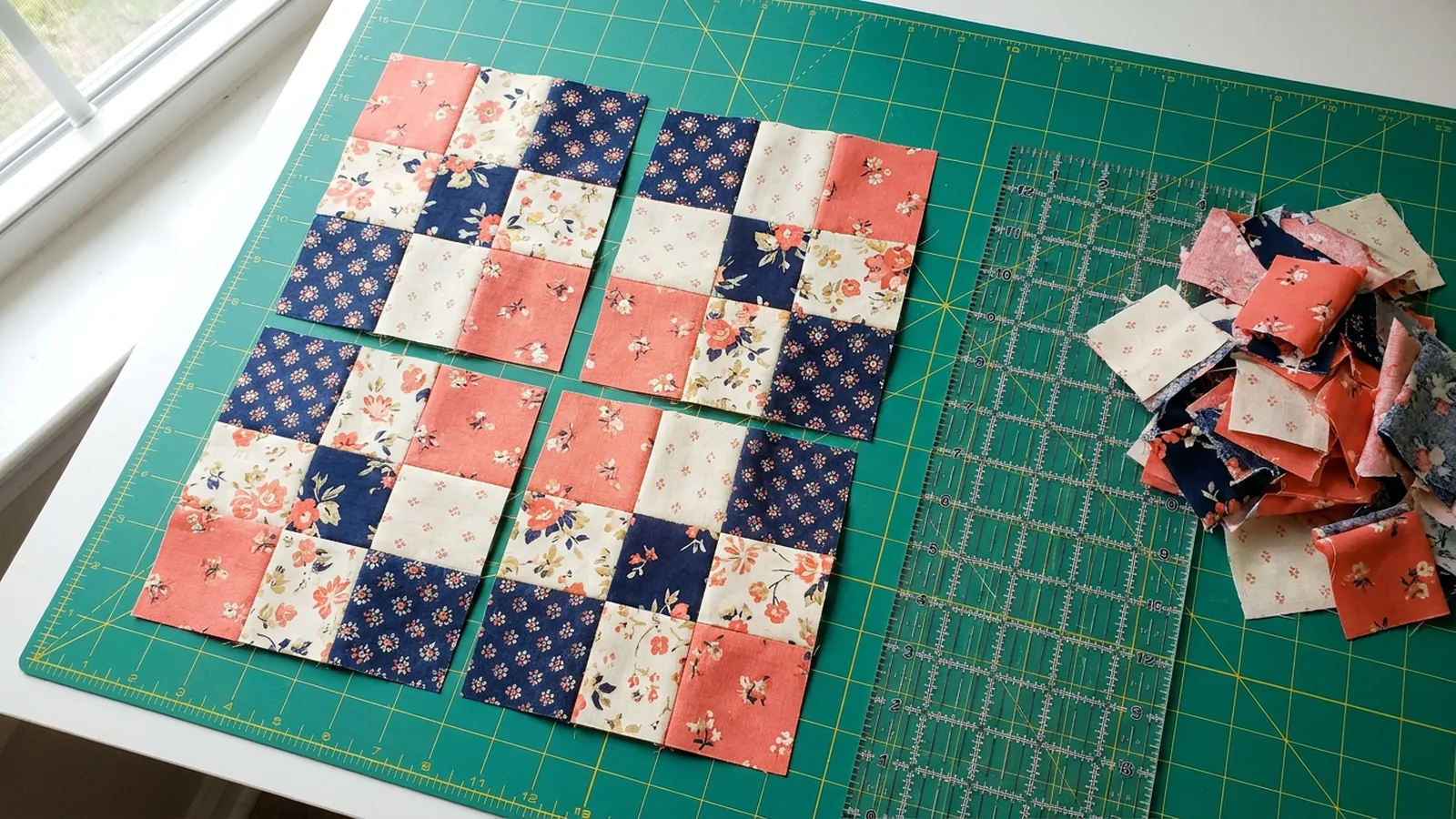 Illustrative generated image of four rearranged nine-patch pieces in coral and navy on a cutting mat beside a quilting ruler.