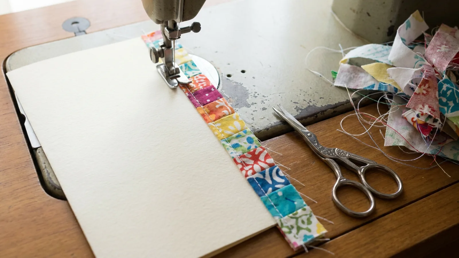 Illustrative generated image of blank paper and a strip of colorful fabric under a sewing machine needle, with scissors nearby.