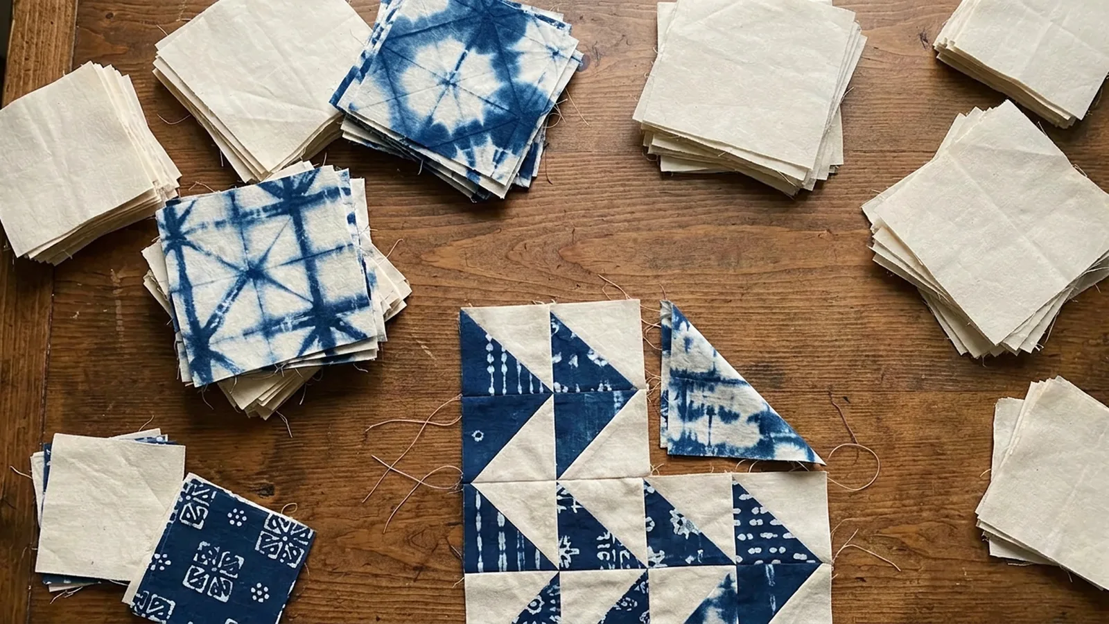 Illustrative generated image of cream and indigo cotton squares and a partly pieced triangle quilt top on a wooden table.
